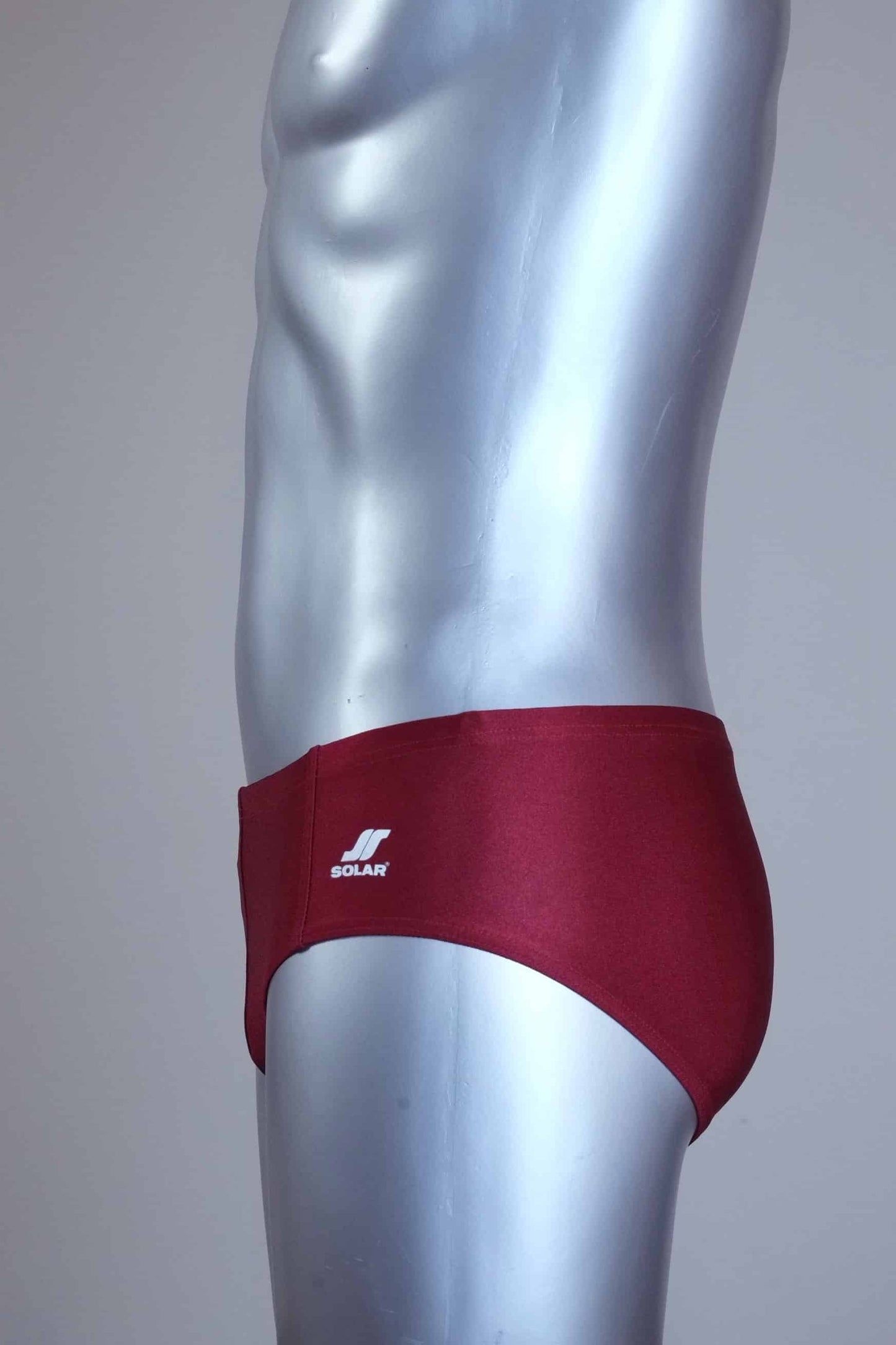 Side view of a mannequin wearing a pair of vintage 70s burgundy swim briefs with a visible brand logo on a gray background