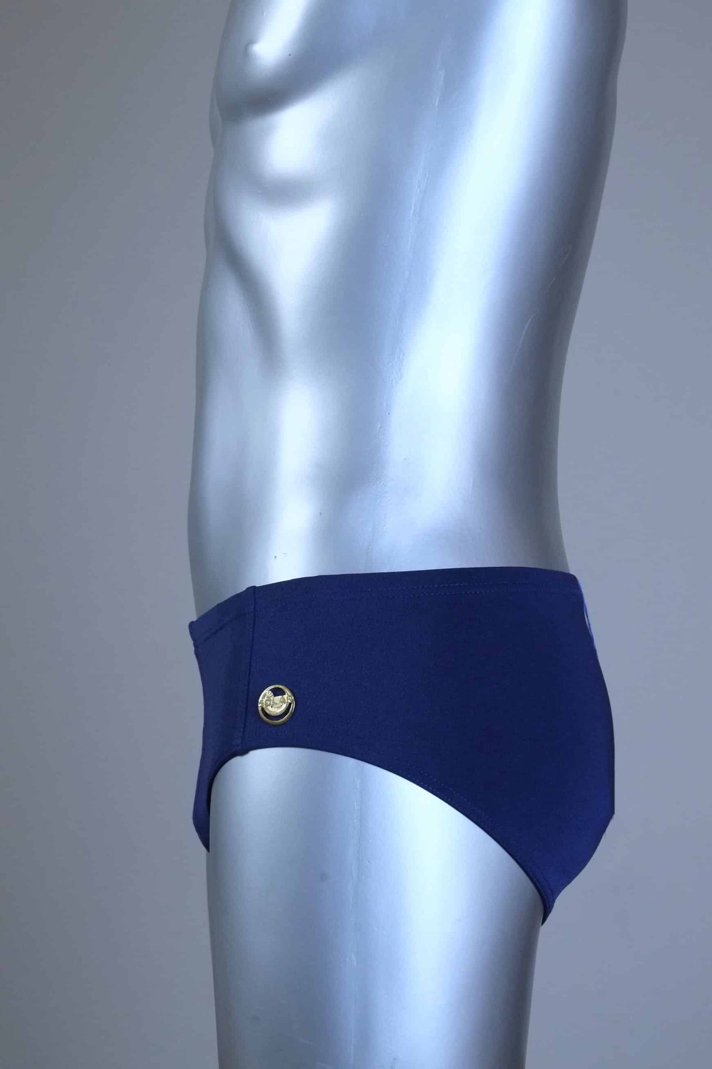 Side view of a mannequin wearing a pair of vintage 70s navy swim briefs with a visible brand logo on a gray background