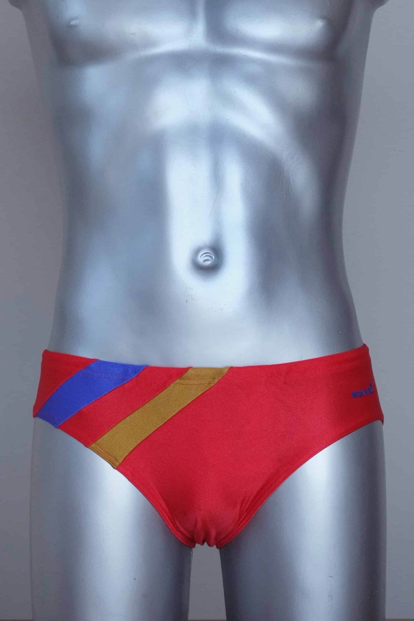 Vintage solar red men's swim briefs with red and yellow stripes on a silver mannequin against a grey background.