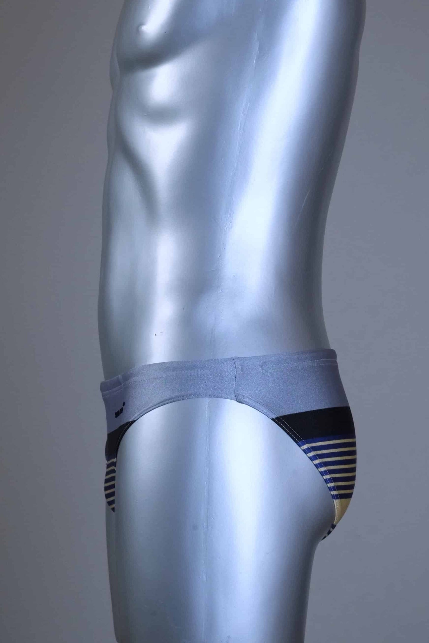 Side view of a Vintage gray and black striped men's swim briefs with brand logo on a metallic mannequin against a gray background