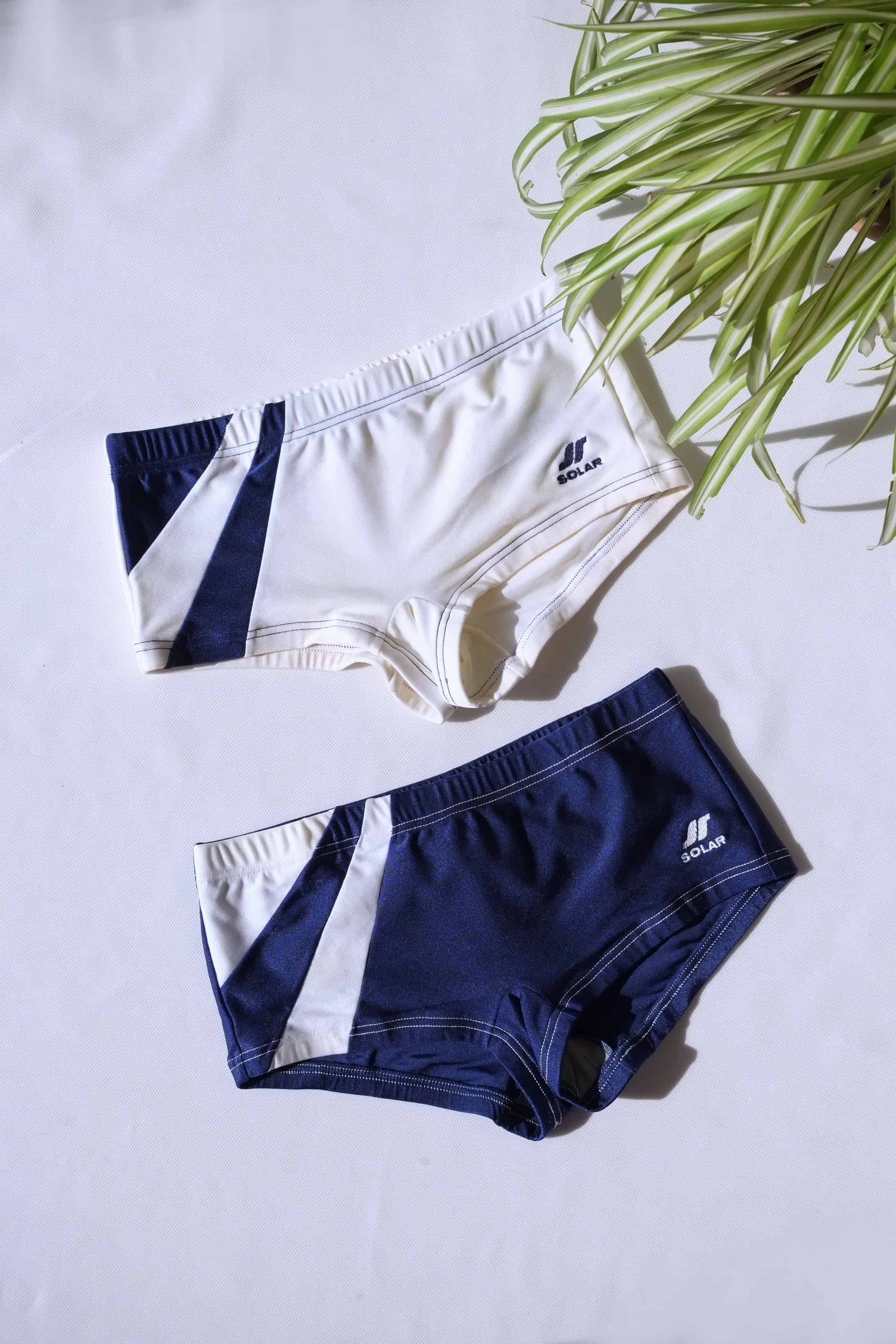 Two pairs of SOLAR brand vintage 80s men's square-cut swim briefs: one off-white with navy diagonal block, the other navy with white diagonal block, laid flat on a white background..