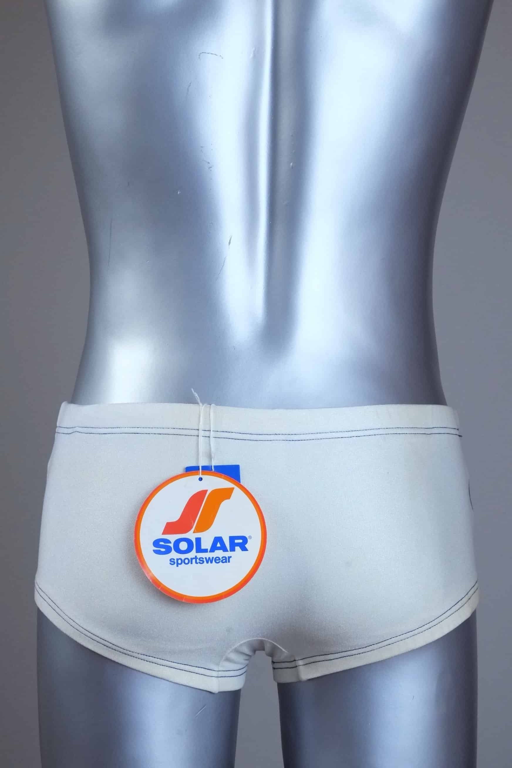 Back view of Vintage white swim briefs on a silver mannequin against a gray background with Solar Sportswear label.