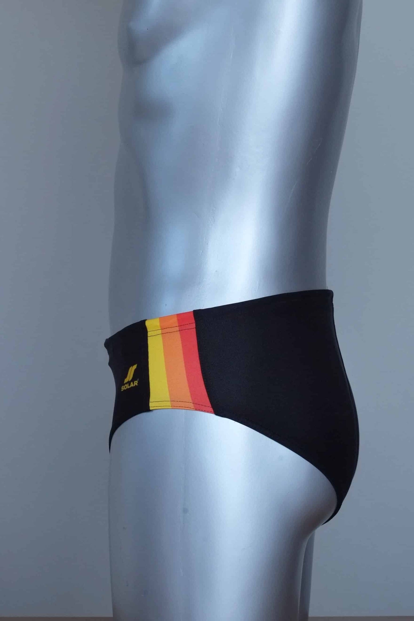 Side view of vintage black swim briefs with colorful side band on a mannequin against a gray background