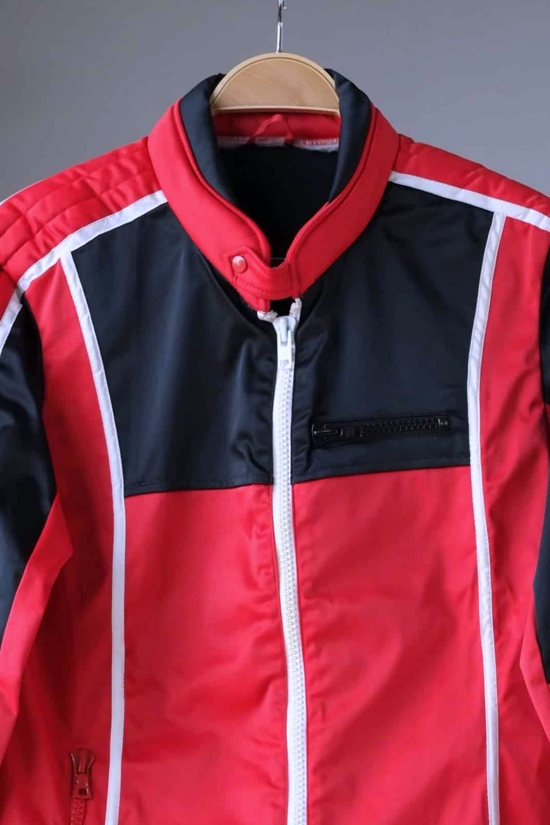 Close-up of the collar and upper body of a vintage Sportalm ski jacket. The jacket features a red and black color-blocked design with white piping and a stand-up collar.