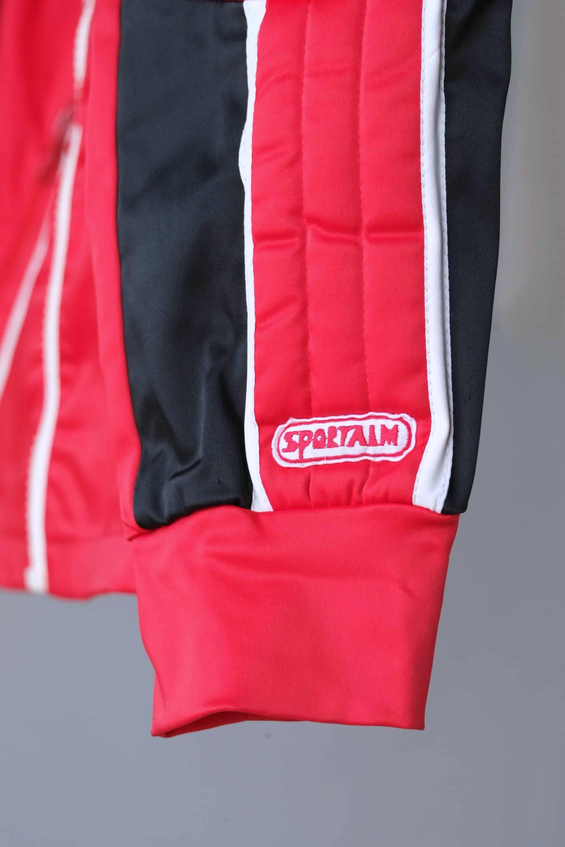 Detail of the Sportalm logo embroidered on the sleeve of a red and black vintage ski jacket.