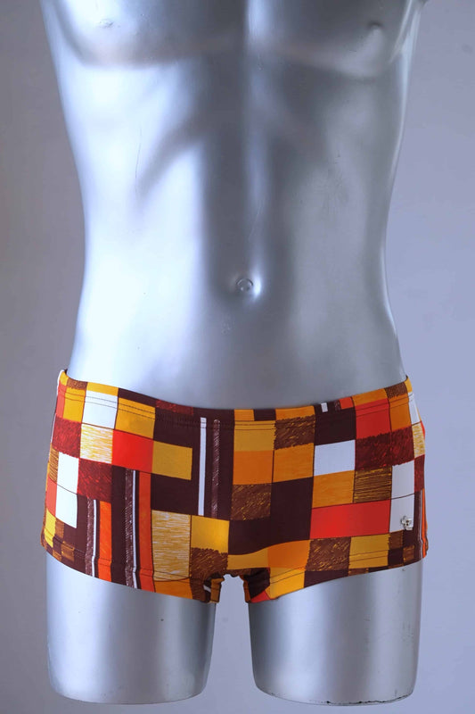 A plastic mannequin wearing a pair of Vintage Tropic swim briefs featuring a retro checkered pattern in orange, red, brown, and white.