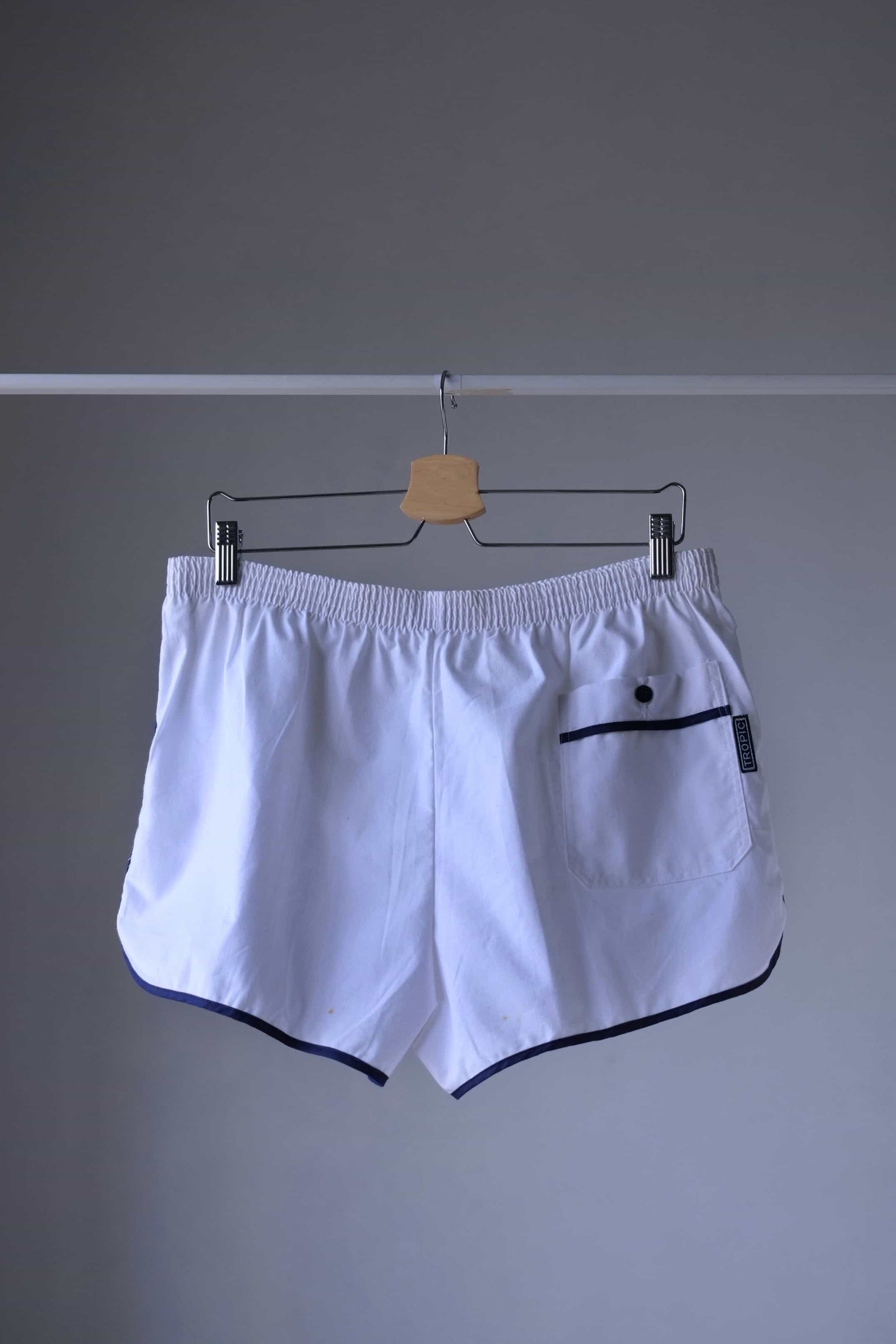 TROPIC Vintage Men's White Shorts displayed on a hanger, viewed from the backside, showing an elastic waistband and a back pocket with navy blue trim.