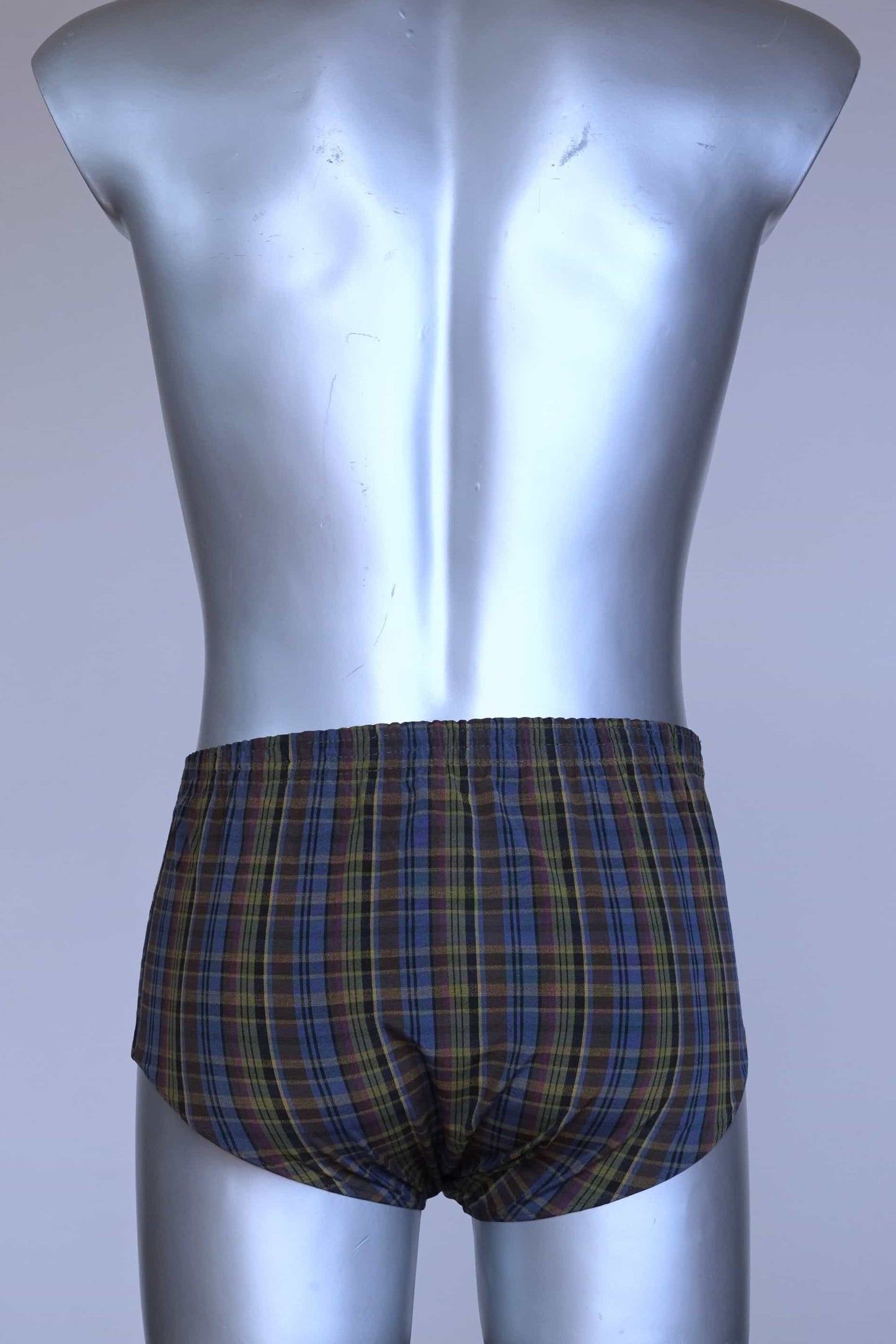 Back view of a vintage late 1950s to early 1960s men's swim brief on a silver mannequin. The brief features a plaid pattern in dark brown, blue, and yellow tones, with a small front flap pocket.