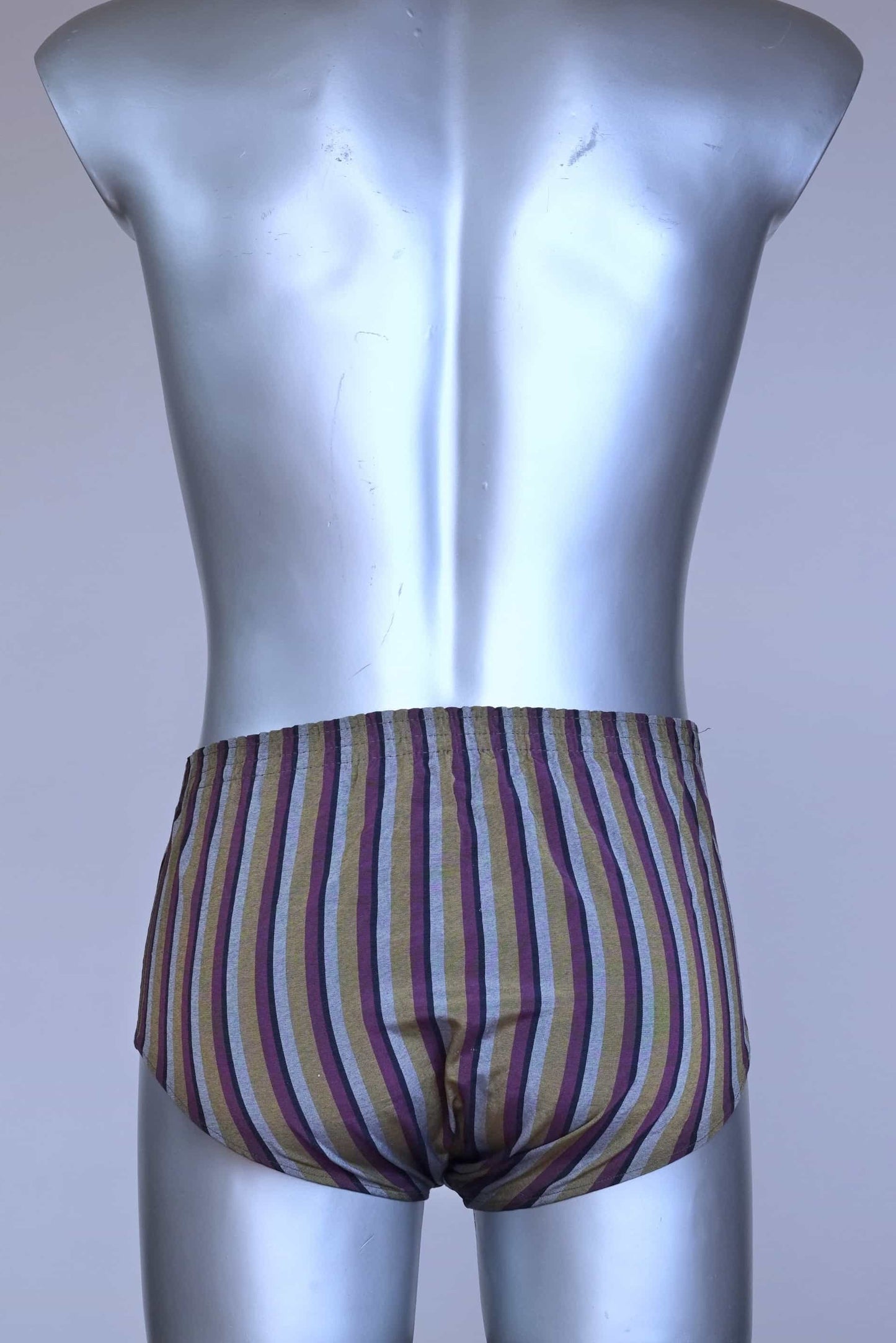 Back view of a vintage late 1950s to early 1960s men's swim brief on a silver mannequin. The brief features vertical stripes in muted brown, grey, and maroon tones, with a small front flap pocket.