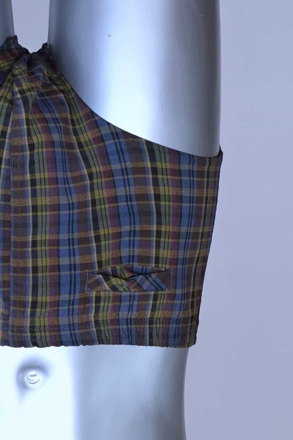 Close view of a vintage late 1950s to early 1960s men's swim brief on a silver mannequin. The brief features a plaid pattern in dark brown, blue, and yellow tones, with a small front flap pocket.
