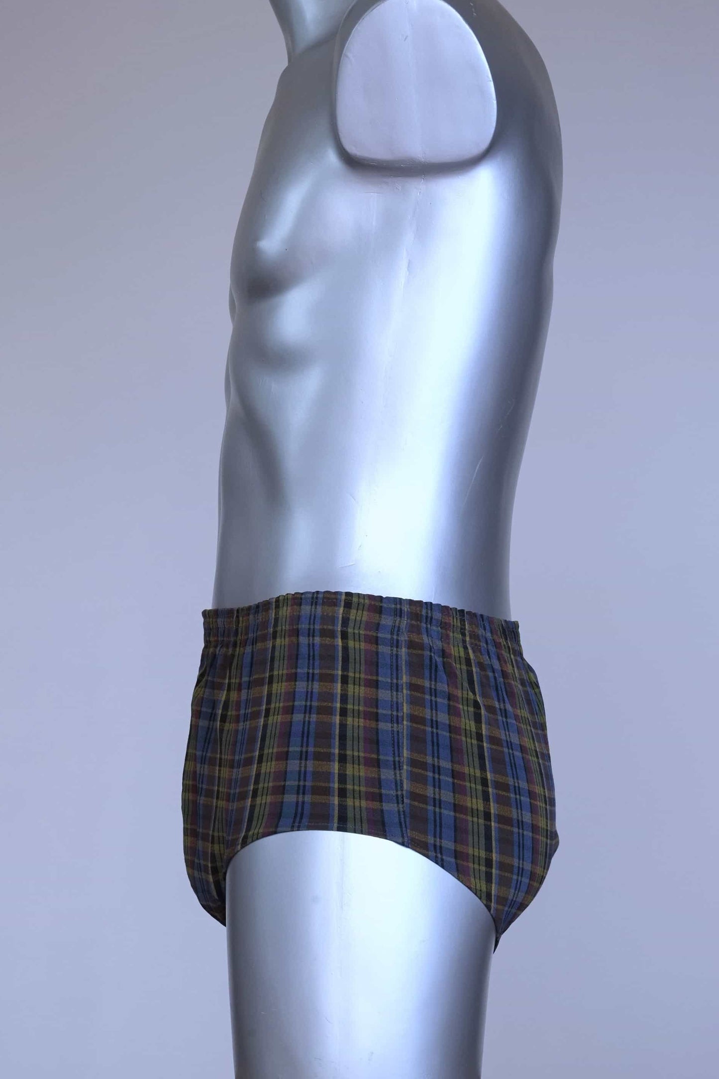 Side view of a vintage late 1950s to early 1960s men's swim brief on a silver mannequin. The brief features a plaid pattern in dark brown, blue, and yellow tones, with a small front flap pocket.