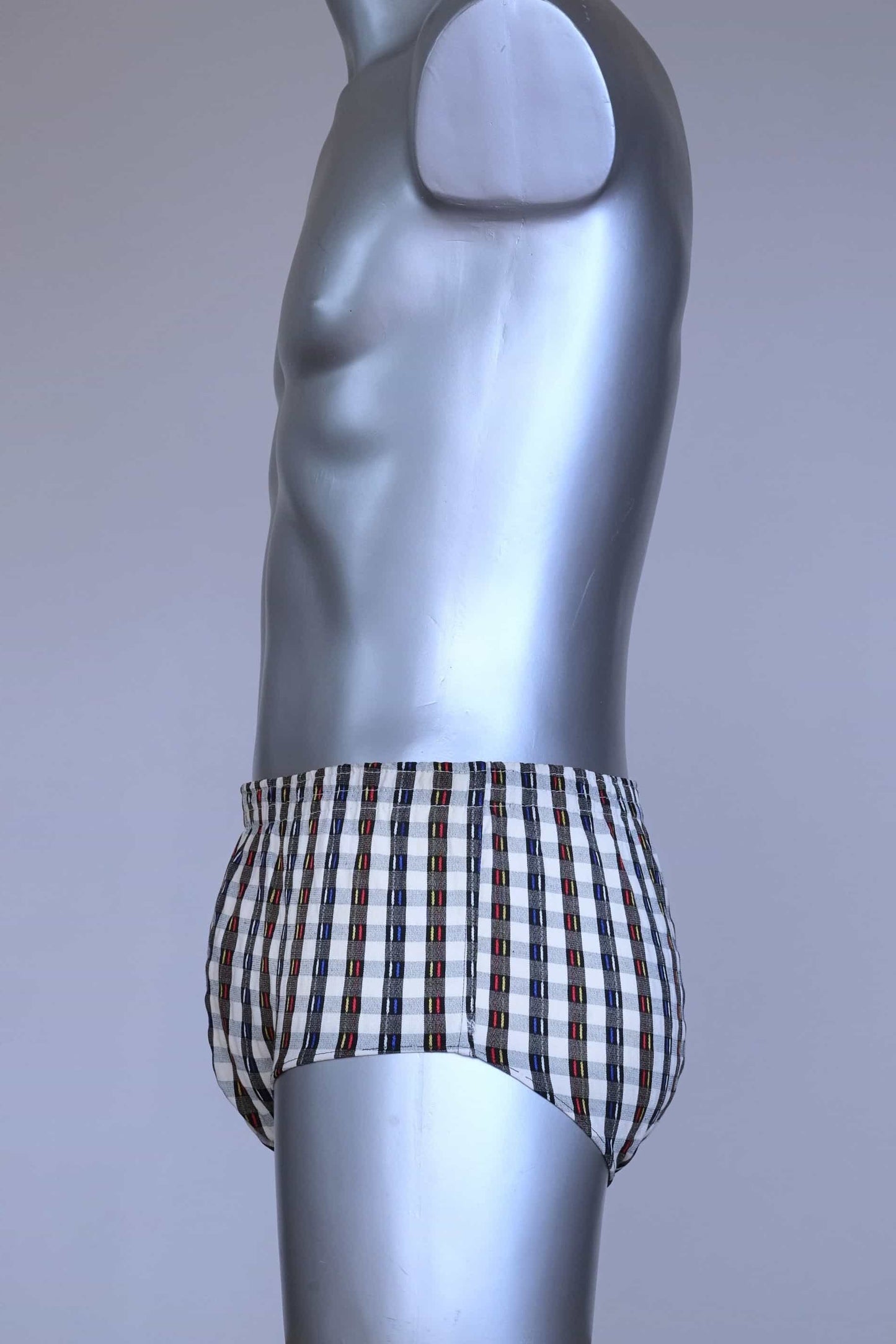 Side view of a vintage late 1950s to early 1960s men's swim brief on a silver mannequin. The brief features a plaid pattern in white, blue, and red, with a small front flap pocket.