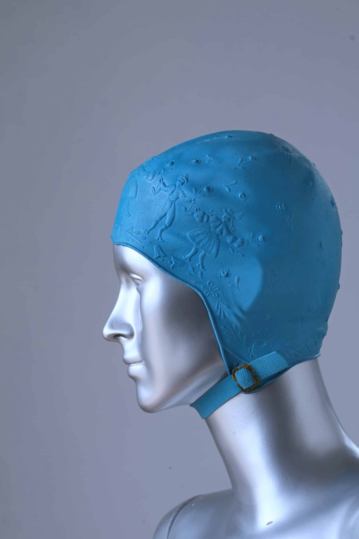 A mannequin wearing a vintage blue swim cap in a pattern depicting children playing.