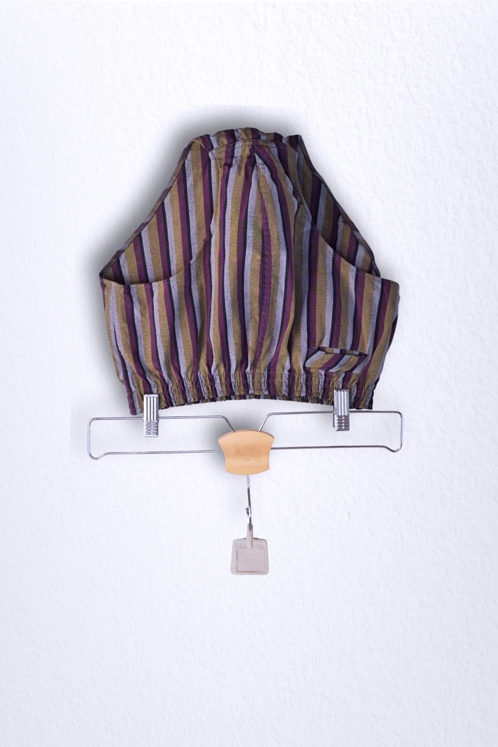 Front view of a vintage late 1950s to early 1960s men's swim brief on a hanger. The brief features vertical stripes in muted brown, grey, and maroon tones, with a small front flap pocket.