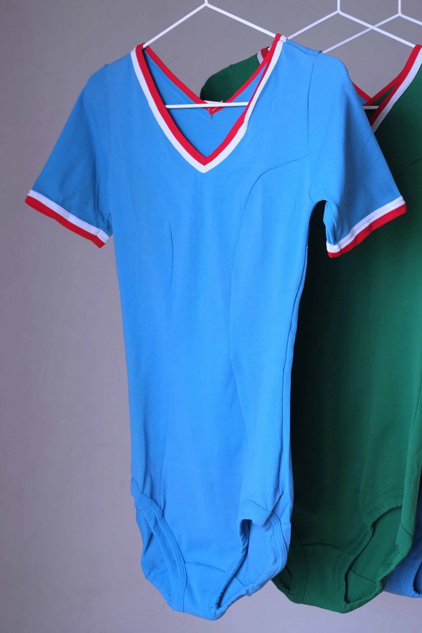 Blue vintage 70s short sleeve leotard with white and red trim, hanging on a rack.
