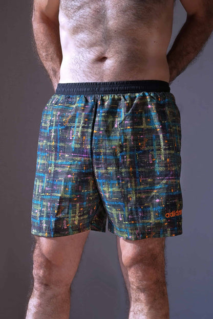 A single ADIDAS vintage 2000s men's abstract print swim short shown on a model from the front. The shorts have a black base with multi-colored speckled lines and an orange ADIDAS logo on the left leg.