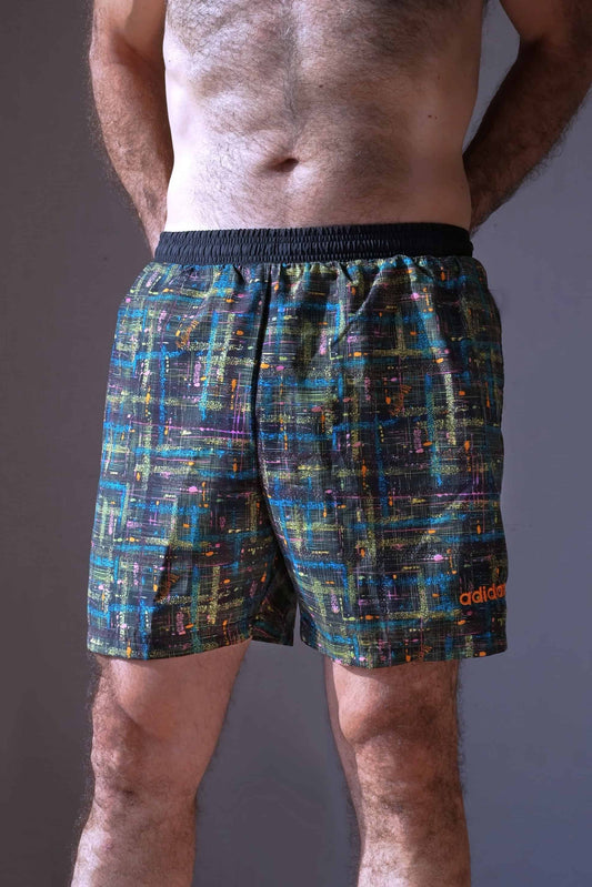 A single ADIDAS vintage 2000s men's abstract print swim short shown on a model from the front. The shorts have a black base with multi-colored speckled lines and an orange ADIDAS logo on the left leg.