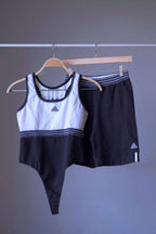 A vintage ADIDAS black and white bodysuit and a pair of black shorts with white stripes, displayed together on hangers.