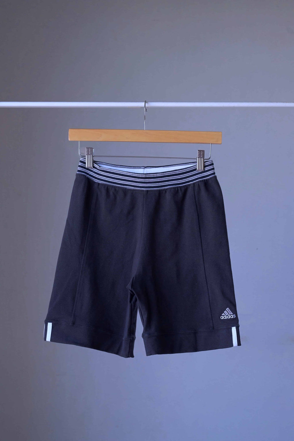 A pair of vintage ADIDAS black shorts with white stripes and an embroidered logo, on a hanger.