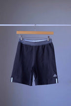 A pair of vintage ADIDAS black shorts with white stripes and an embroidered logo, on a hanger.