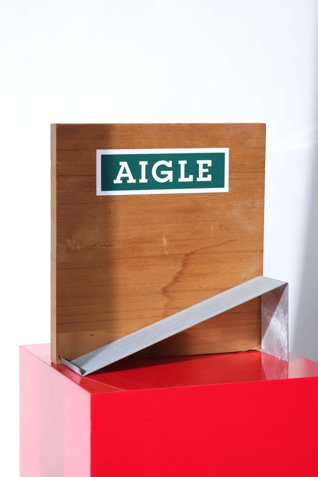 Empty vintage Aigle boot display stand. Wood backboard with green Aigle logo, metal boot ramp.