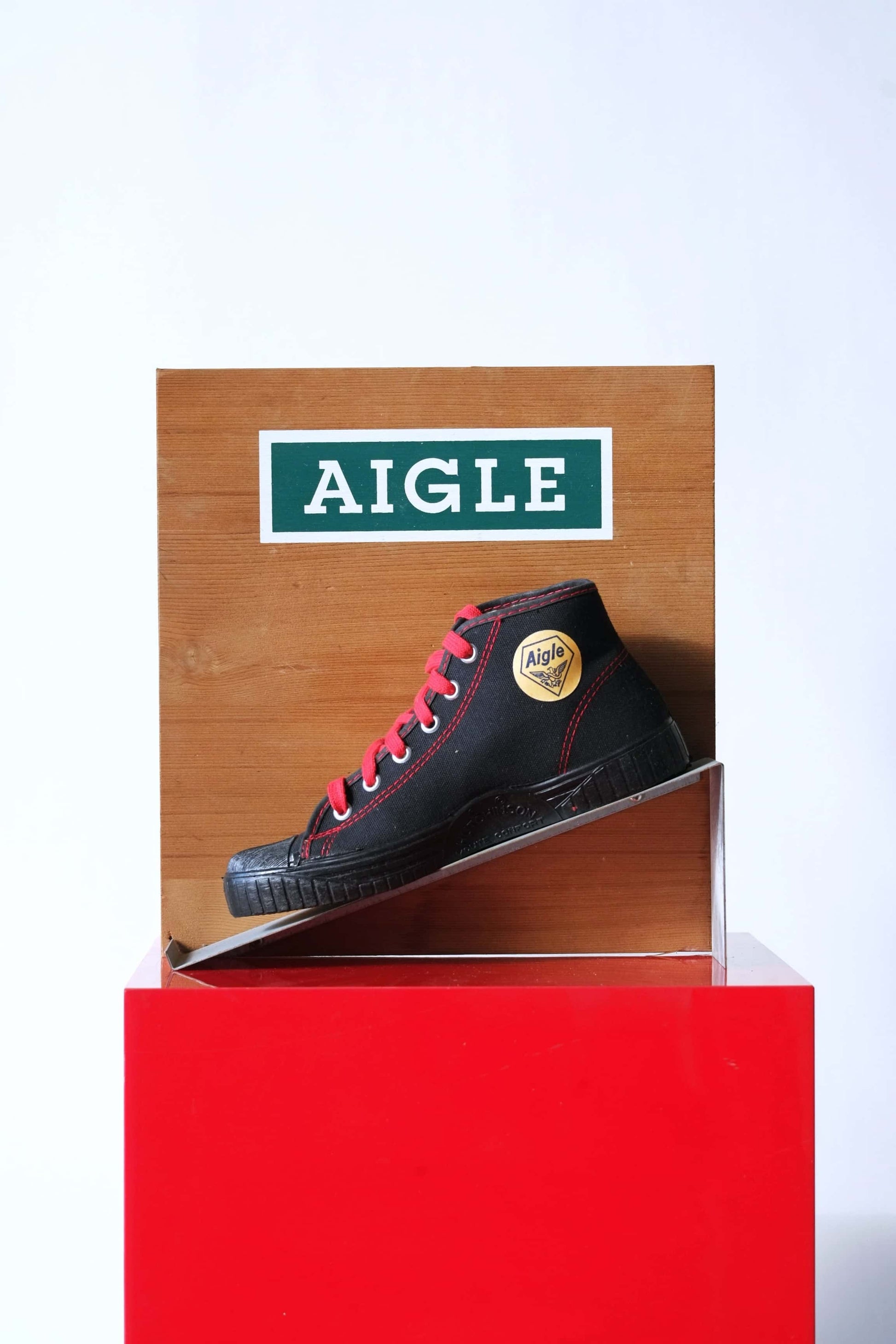 Vintage Aigle boot display stand. Wood with Aigle logo, metal ramp holding a black canvas shoe with red laces.