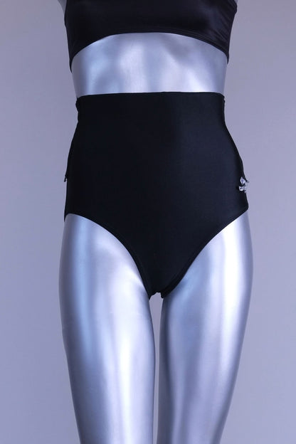 A pair of black, high-rise dance briefs with a folded-over waistband and a logo on the left hip, displayed on a mannequin.