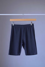 A pair of black vintage 90s Anniel cotton biker shorts hanging on a wooden hanger against a grey background.