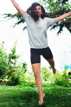 A person jumping outdoors on green grass, wearing a grey sweatshirt and black vintage 90s Anniel cotton biker shorts.