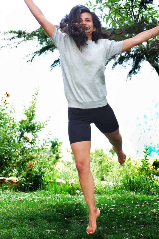 A person jumping outdoors on green grass, wearing a grey sweatshirt and black vintage 90s Anniel cotton biker shorts.