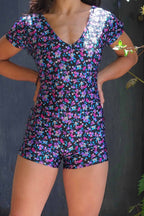 A person modeling an ANNIEL vintage 90s floral print activewear biketard with short sleeves and a V-neck, standing against a dark background.