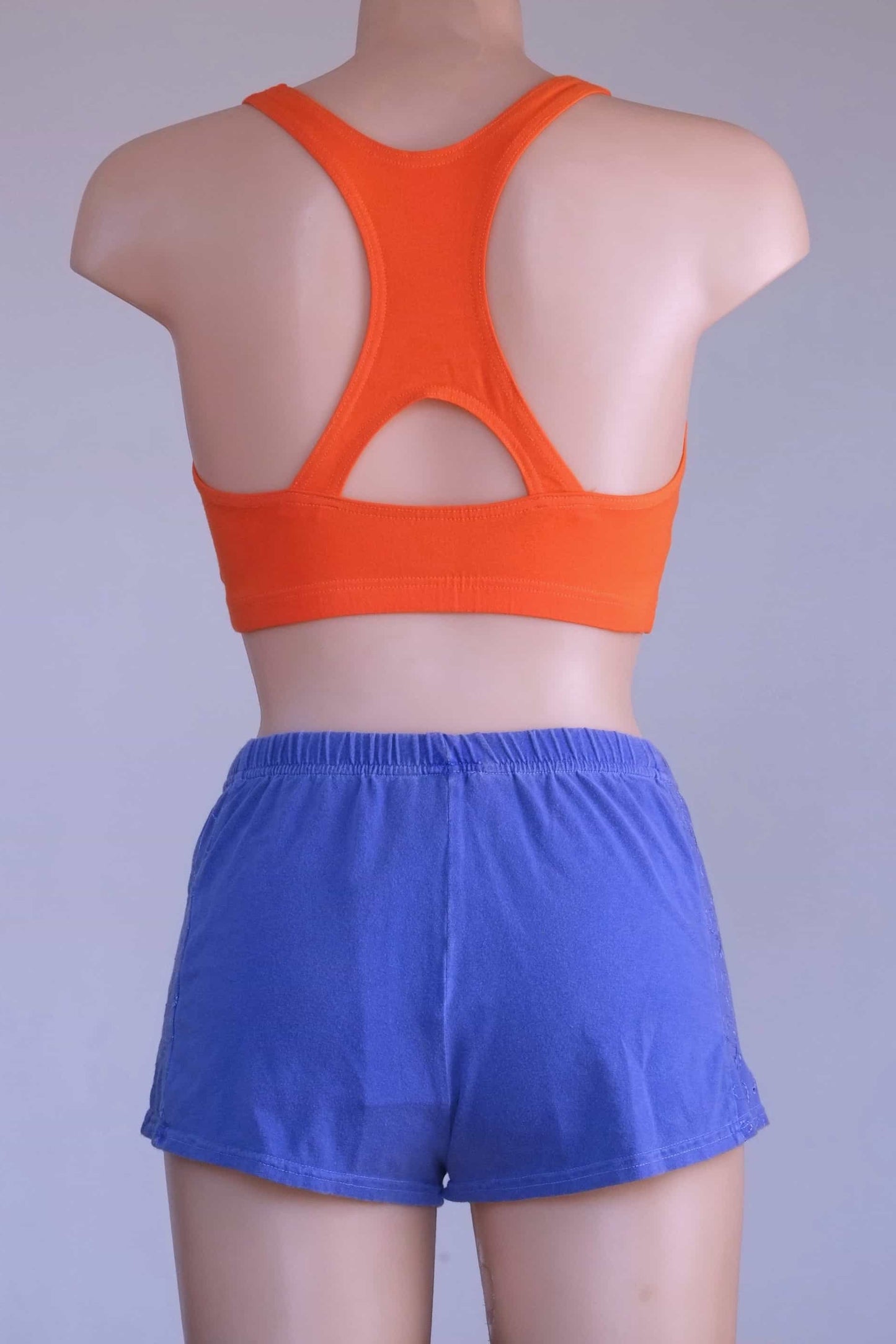 Back view of a mannequin wearing a Vintage 90s Anniel orange racerback sports bra and blue shorts, highlighting the keyhole detail.