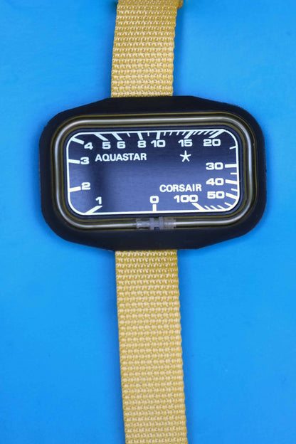 Close shot of A vintage Aquastar Corsair analog depth gauge with a black rectangular dial, encased in a black frame. The depth gauge is attached to a vibrant yellow band and is displayed against a blue background. The dial features white markings and numbers, measuring depths up to 100 meters.