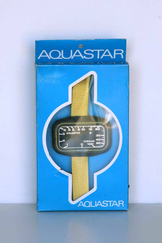 Front view of a vintage Aquastar Corsair depth gauge in its original blue packaging. The gauge, with a black face and white markings, is displayed prominently through a transparent cutout. It features a yellow strap and depth measurements up to 100 meters. The Aquastar logo is visible on both the gauge and the packaging, emphasizing the brand's identity. The packaging shows slight wear, adding to its vintage appeal.