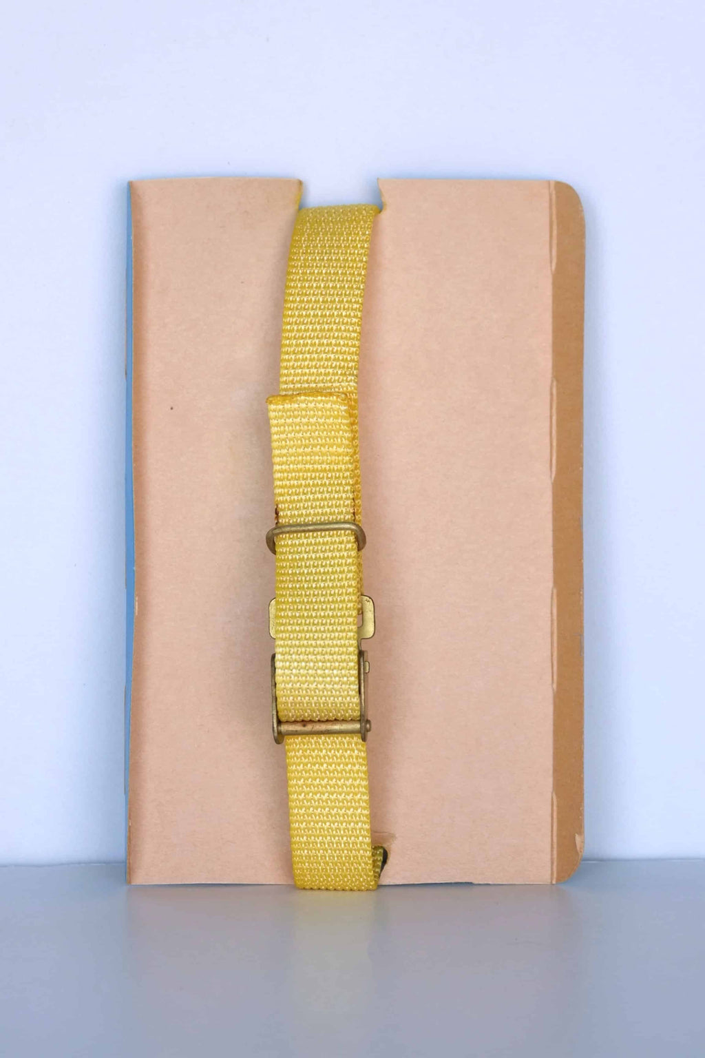 The back view of a vintage Aquastar Corsair depth gauge, featuring a yellow adjustable strap with a metal buckle. The strap is displayed against a neutral brown and blue background, highlighting the simplicity and functionality of the wristband. The depth gauge itself is not visible from this angle, focusing solely on the strap and its fastening mechanism.