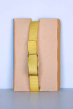 The back view of a vintage Aquastar Corsair depth gauge, featuring a yellow adjustable strap with a metal buckle. The strap is displayed against a neutral brown and blue background, highlighting the simplicity and functionality of the wristband. The depth gauge itself is not visible from this angle, focusing solely on the strap and its fastening mechanism.
