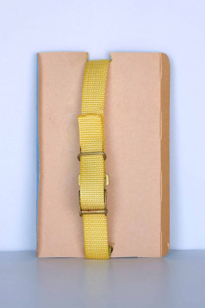 The back view of a vintage Aquastar Corsair depth gauge, featuring a yellow adjustable strap with a metal buckle. The strap is displayed against a neutral brown and blue background, highlighting the simplicity and functionality of the wristband. The depth gauge itself is not visible from this angle, focusing solely on the strap and its fastening mechanism.