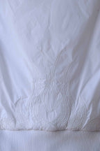 Close-up of the back of a white Y2K-style puffer vest, showcasing intricate flame embroidery with crystal embellishments. The detailed stitching and ribbed hem add a stylish and textured element to this trendy sleeveless vest.