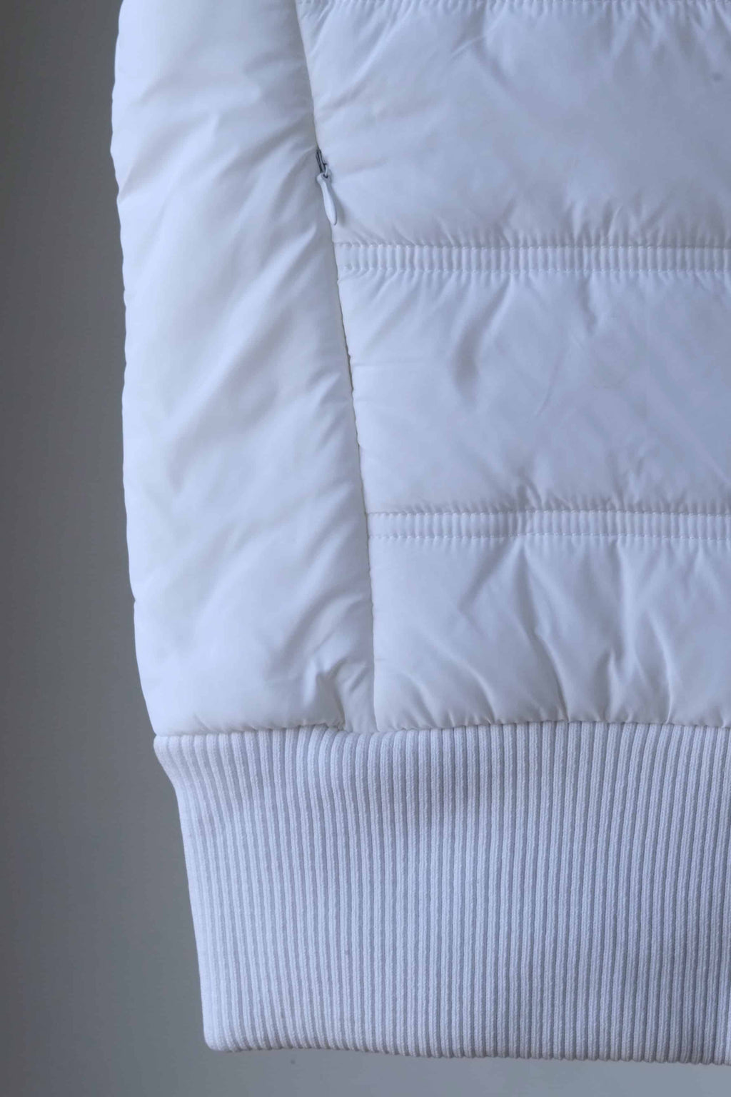 Detail shot of a white sleeveless puffer vest, showcasing the quilted pattern and ribbed hem.