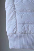 Detail shot of a white sleeveless puffer vest, showcasing the quilted pattern and ribbed hem.