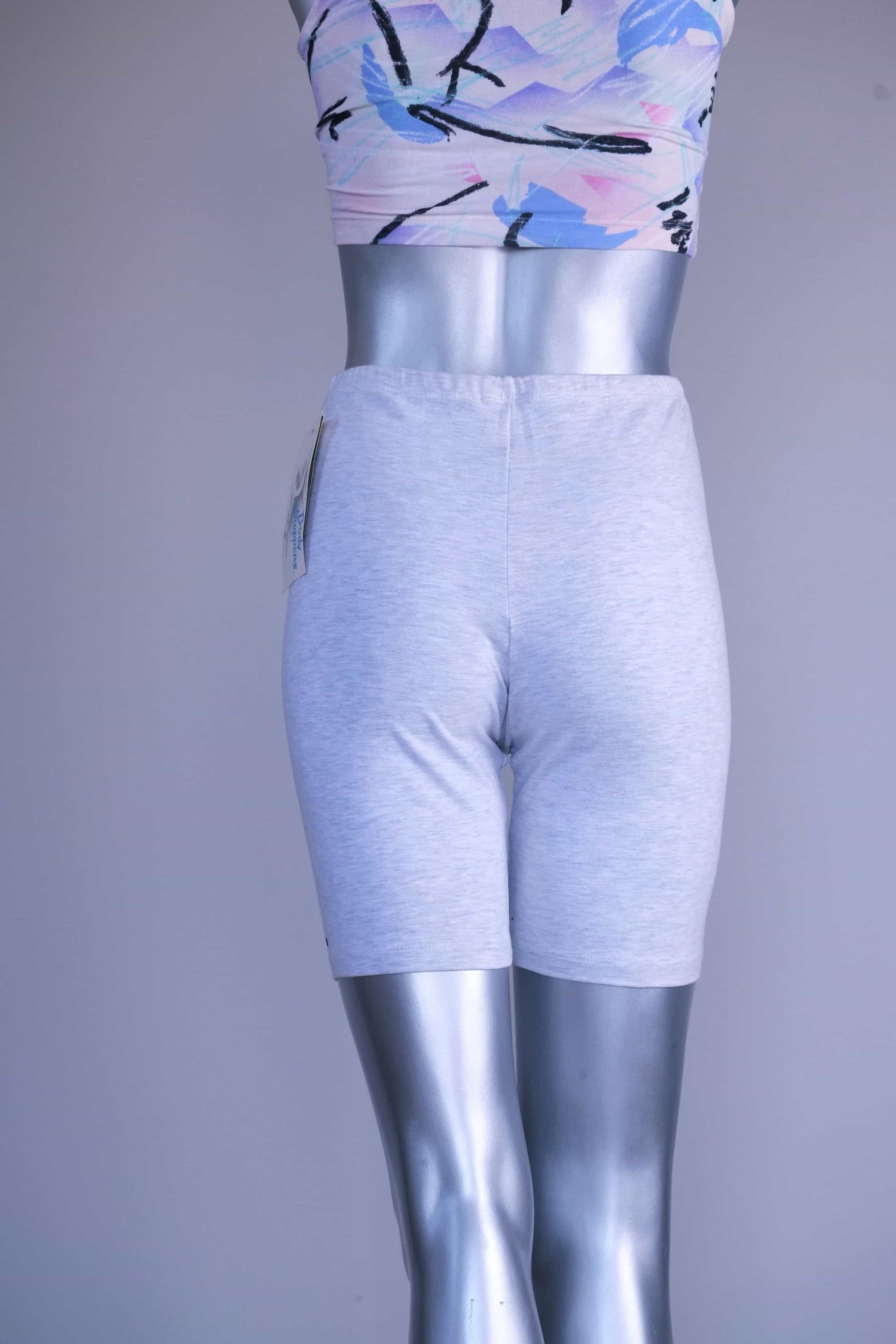 Back view of a mannequin wearing light ash gray vintage 90s BODY WRAPPERS bike shorts and a pastel print crop top.