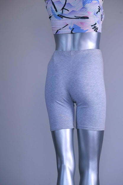 Back view of a mannequin wearing a slightly darker heather gray vintage 90s BODY WRAPPERS bike shorts and a pastel print crop top.