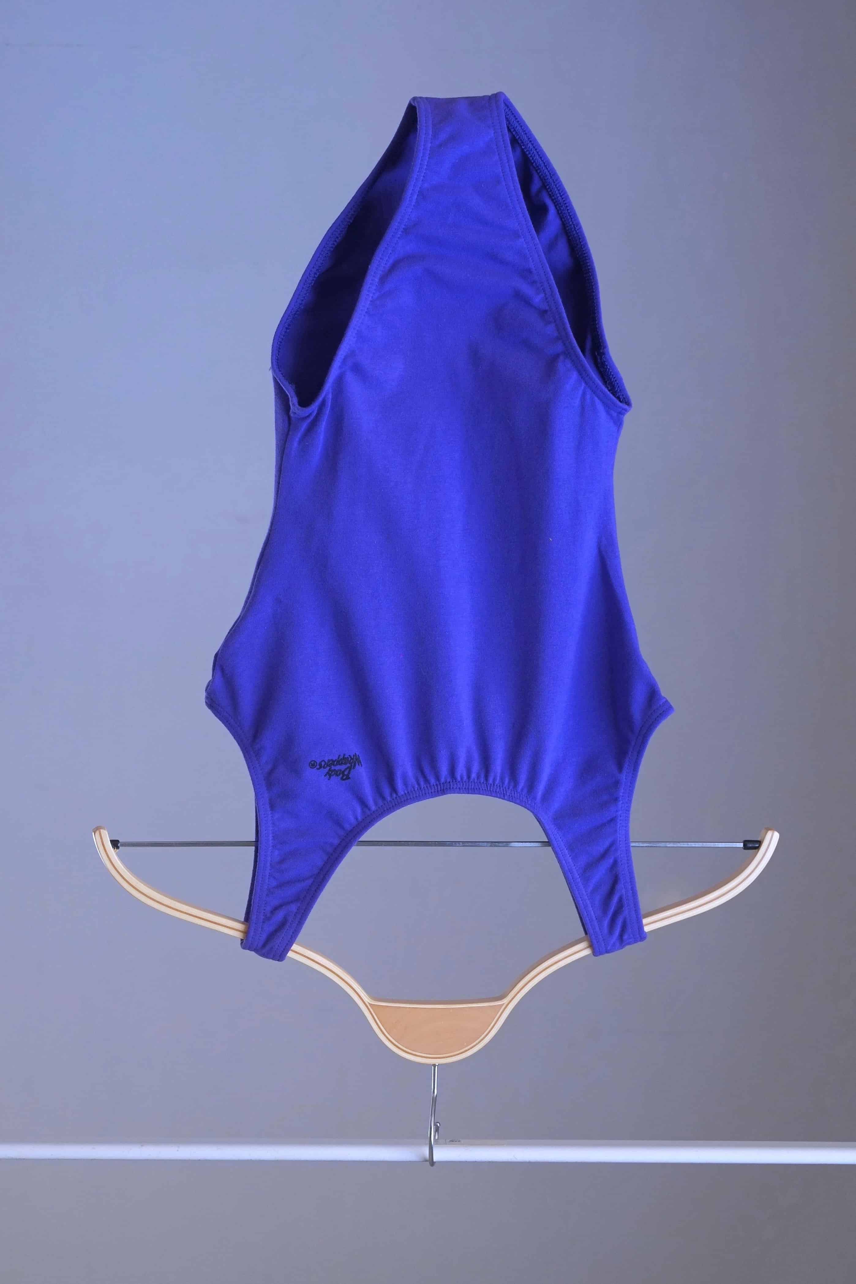 The vintage Body Wrappers leotard in purple, hanging on a clothes rack.