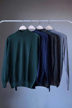 Vintage 90s Cagi pure wool high-neck sweaters in four colors (dark green, navy, heather charcoal, heather grey) hanging on a rail.
