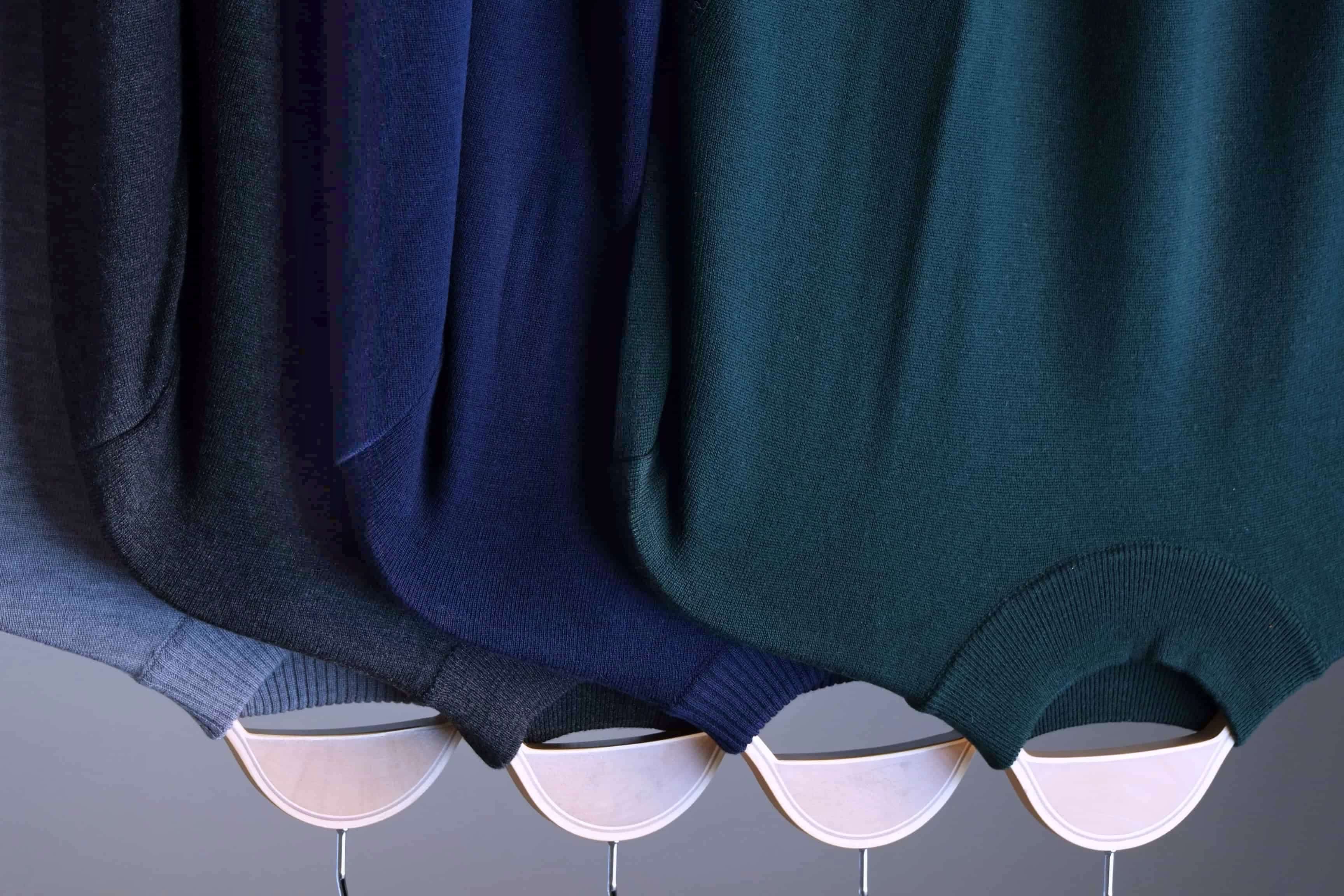 Tight shot showing the high-neck collars of the four Cagi Italian pure wool sweaters (green, navy, charcoal, grey). Note the mix of ribbed and unribbed neck finishes.