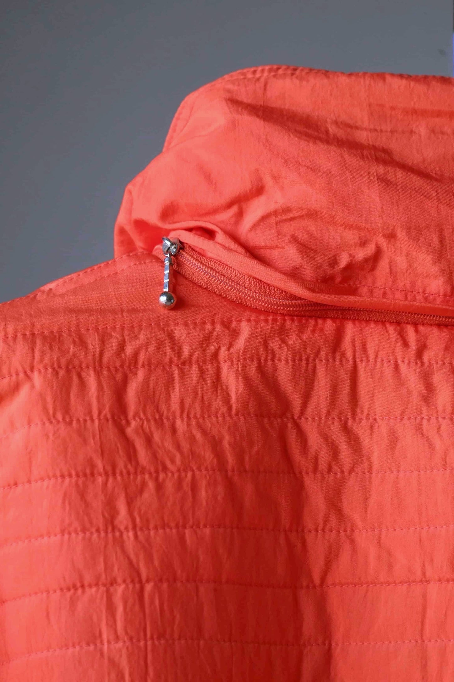 Close-up of the collar and zipper of a vintage orange jacket. The jacket has a high collar with a silver zipper with a decorative pull.