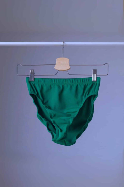 A pair of vintage Danskin high-cut dance briefs in emerald green, hanging on a clothes rack.