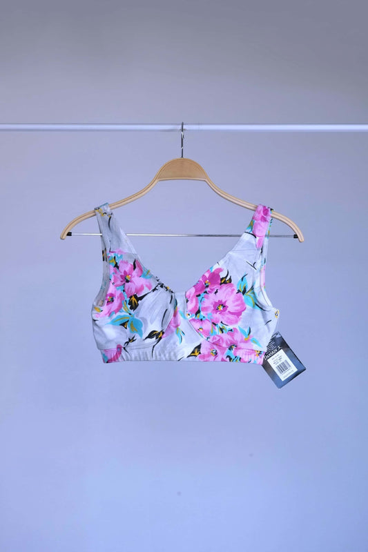 Front view of A vintage 90s Danskin activewear bralette-style crop top with a floral print, hanging on a metal rack.