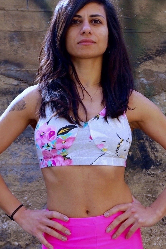 A person modeling a DANSKIN vintage 90s floral print crop top with pink, yellow, and blue flowers, standing against a textured wall.