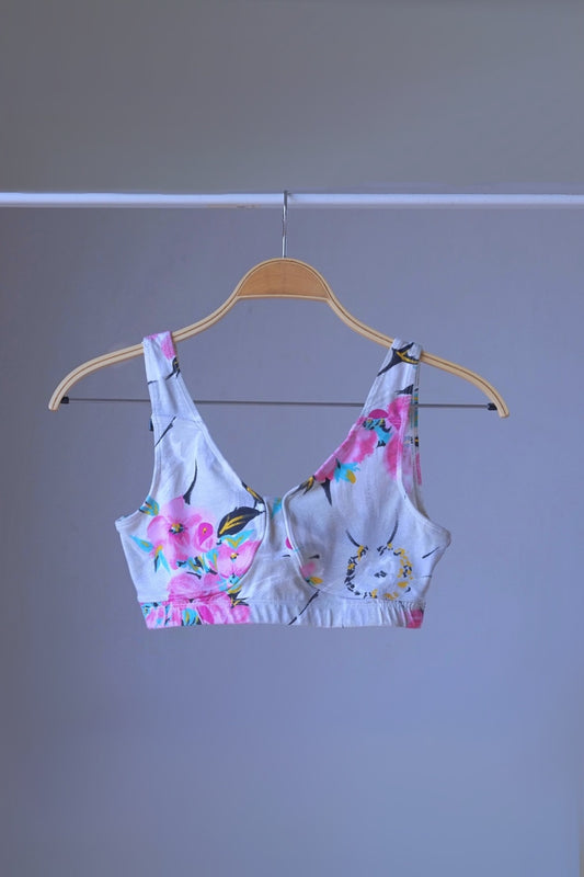 DANSKIN vintage 90s floral print crop top with pink, yellow, and blue flowers on a white background, displayed on a wooden hanger.